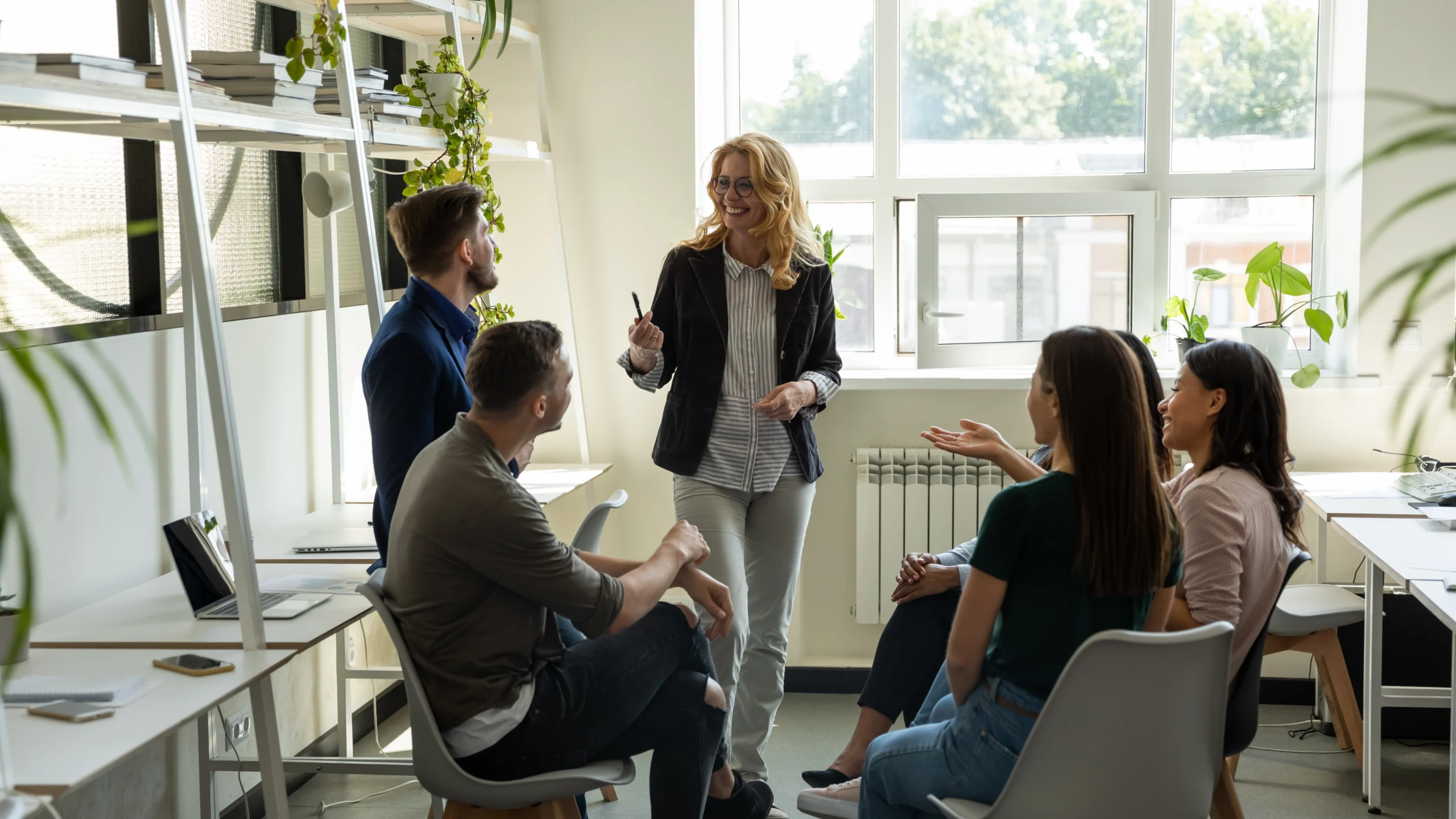 Smiling female leader, coach holding briefing for multiracial team interns in office, teaching students, plan to subordinates. Businesswoman at company meeting with diverse colleagues.