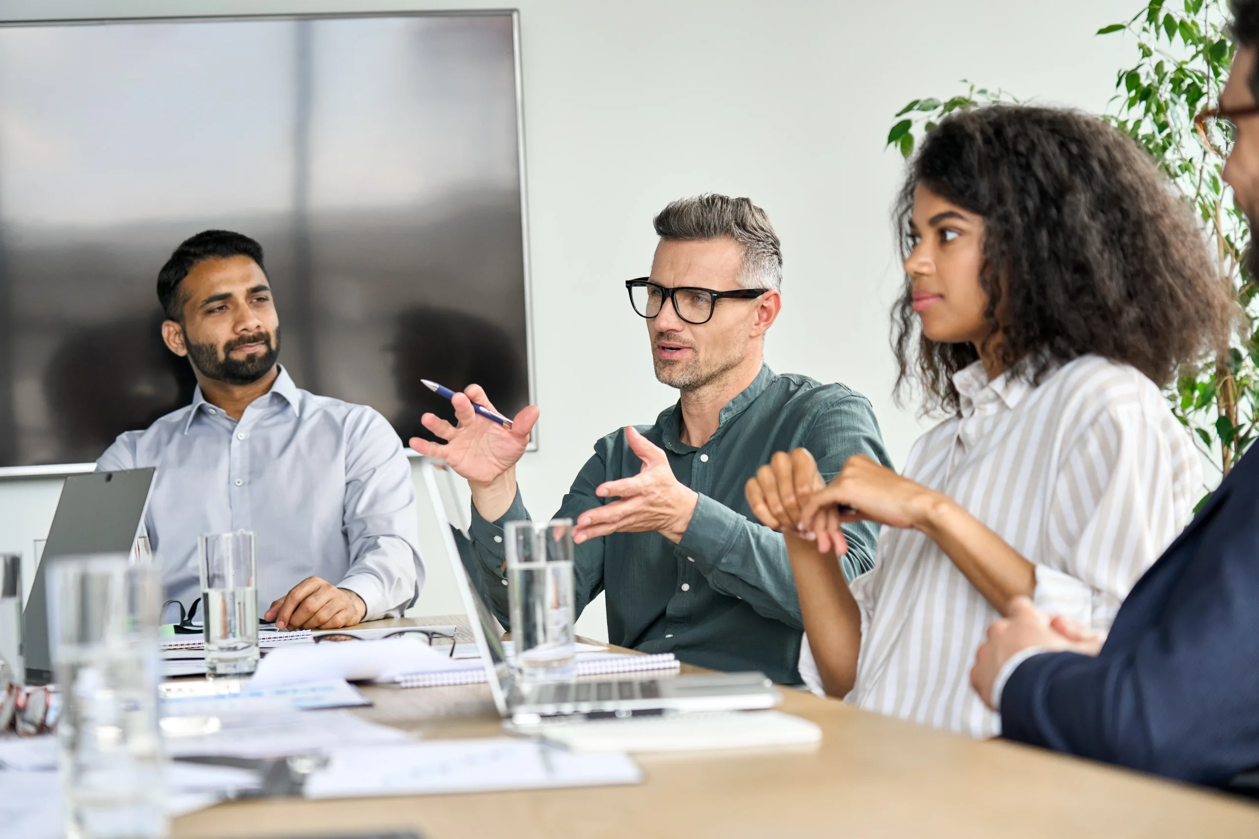 Mature mentor manager speaking at executive team meeting in boardroom. Male leader training executive team at board briefing. Multicultural professional business people discussing strategy in office