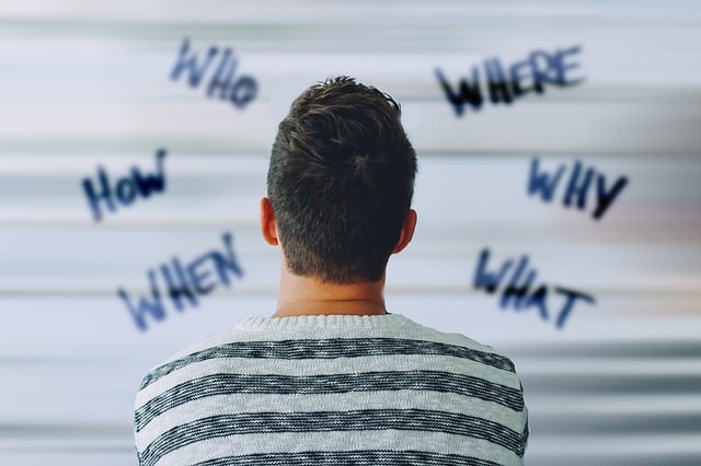 A man seen from behind looking at words such as "Who," "What," "Why," and "When" written on a blurred background.